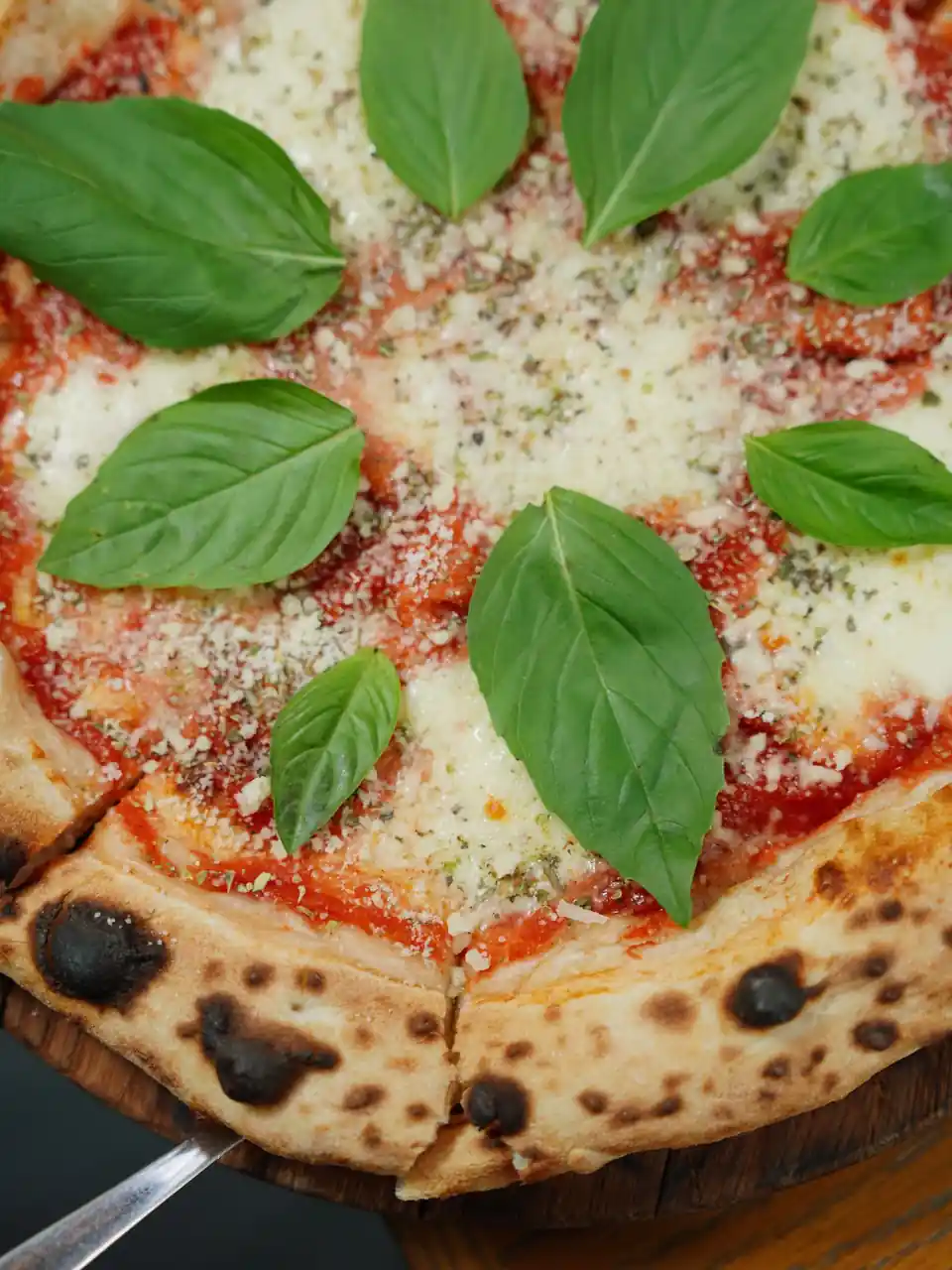 Perinteinen vastapaistettu Margherita-pizza puisella leikkuulaudalla tuoreella basilikalla