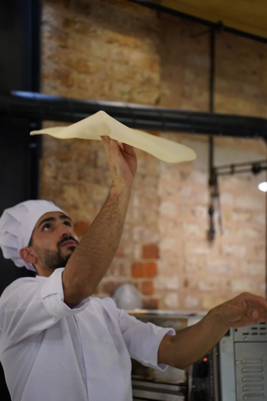 Pizzamestari käsittelee taikinaa käsin ja muotoilee pyöreää pohjaa