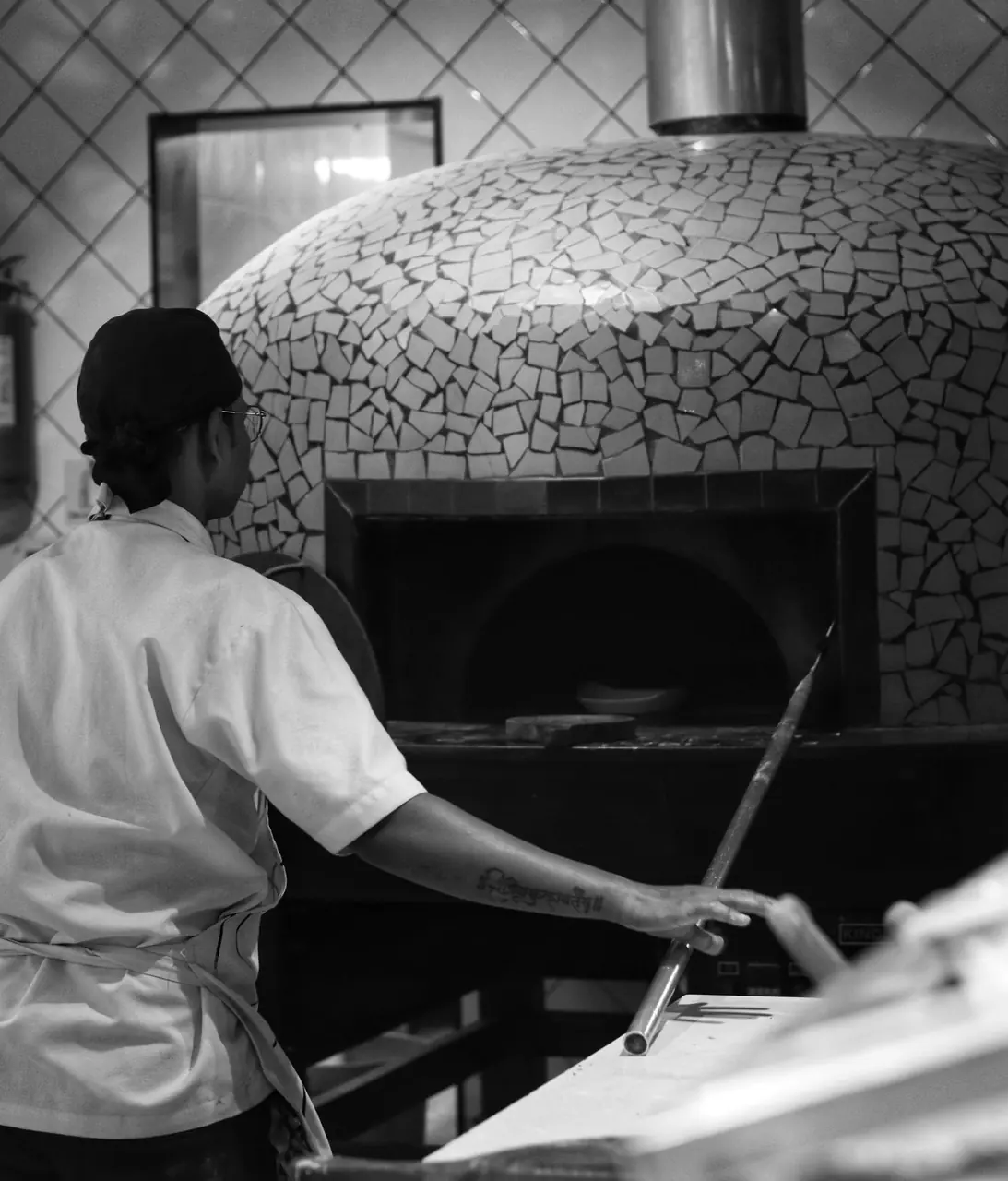 Pizzamestari viimeistelee pizzaa uunin edustalla keittiössä
