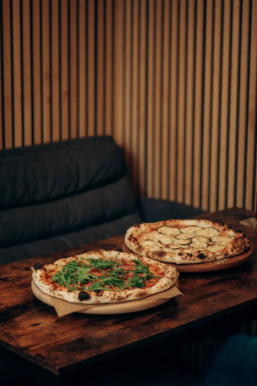 Kaksi erilaista pizzaa katettuna puiseen ruokapöytään valoisassa huoneessa