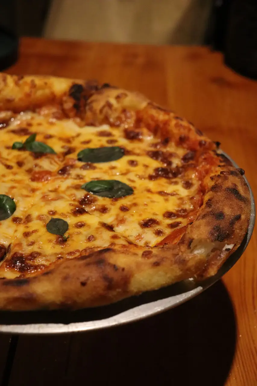 Tuore uunipizza rapealla reunalla ja tuoreella basilikalla puualustalla