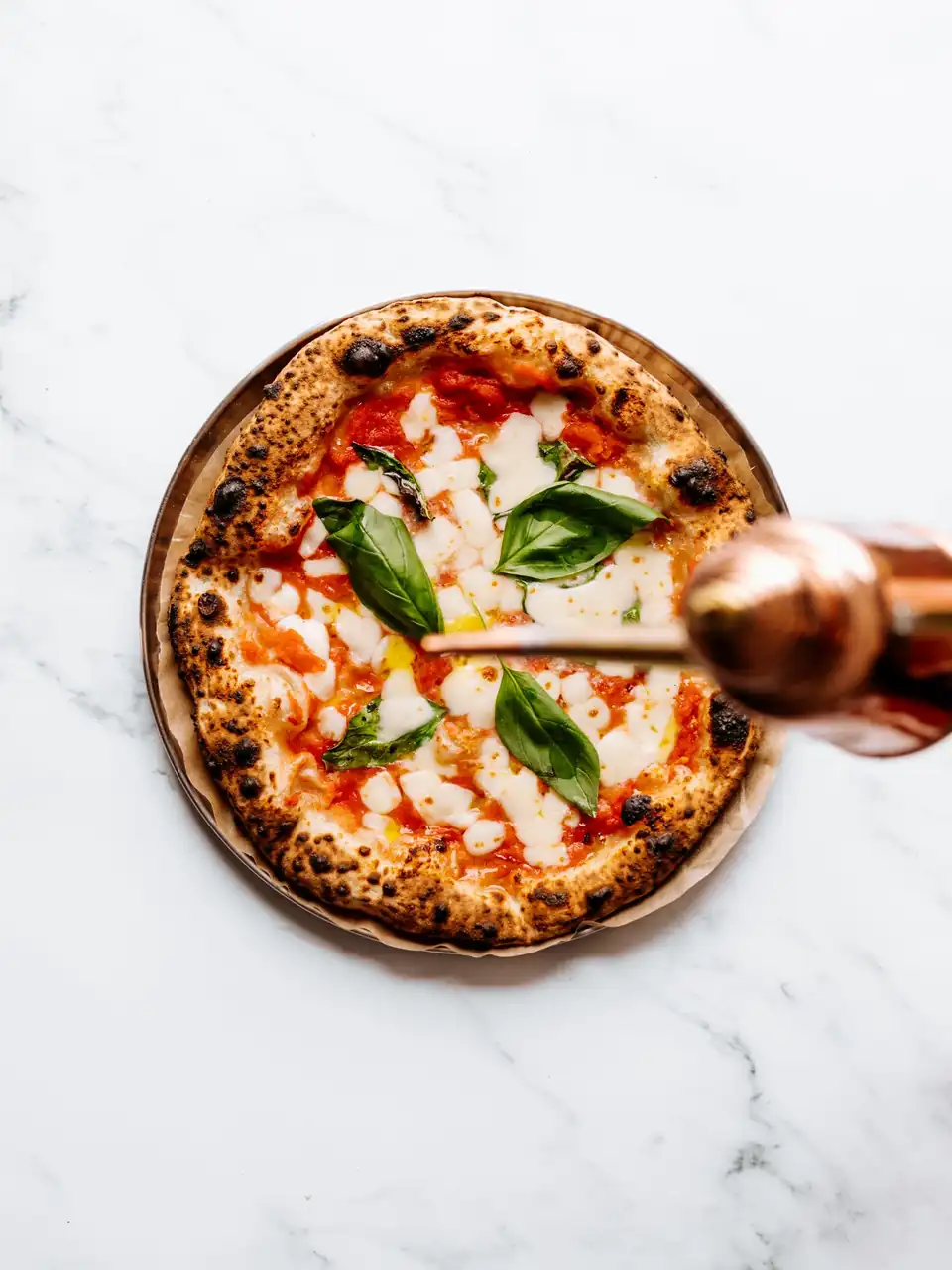 Klassinen pizza marmoripöydällä tuoreilla yrteillä ja oliiviöljyllä