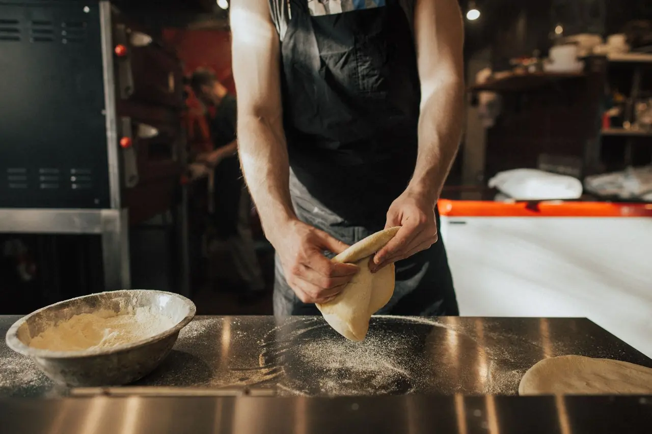 Pizzakokki vaivaamassa tuoretta taikinaa jauhotetulla puisella pöydällä keittiössä