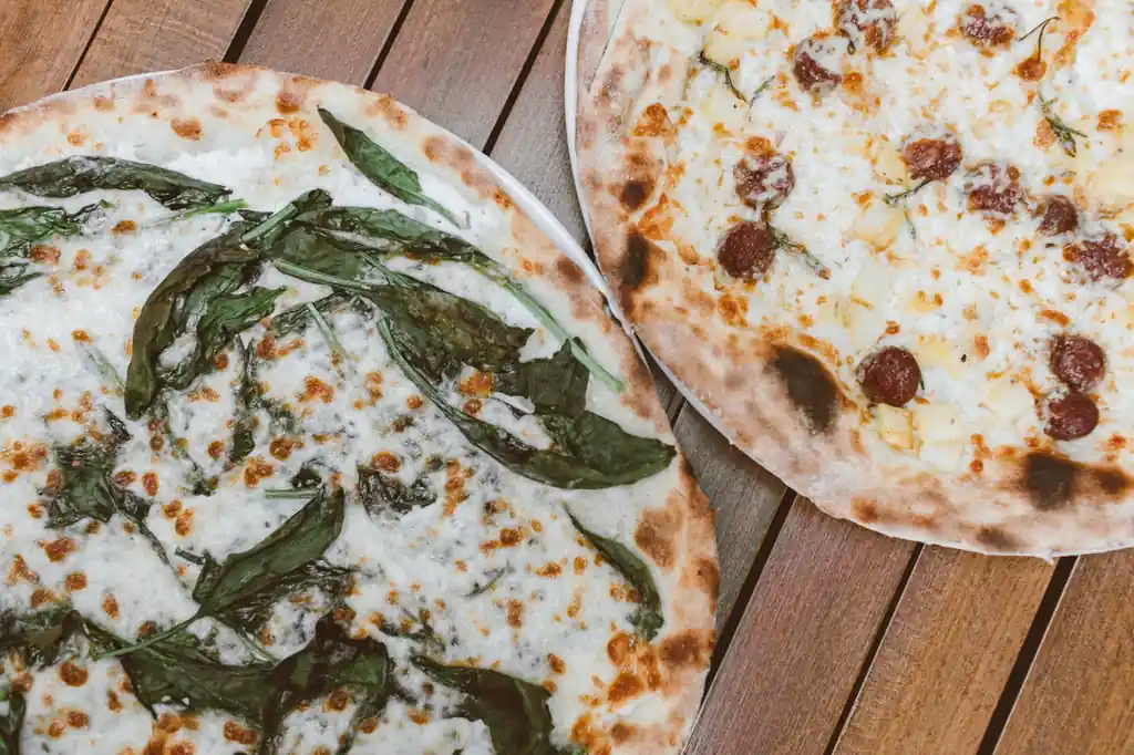 Lähikuva tuoreista täytteistä ja rapeasta pizzapohjasta puupöydällä